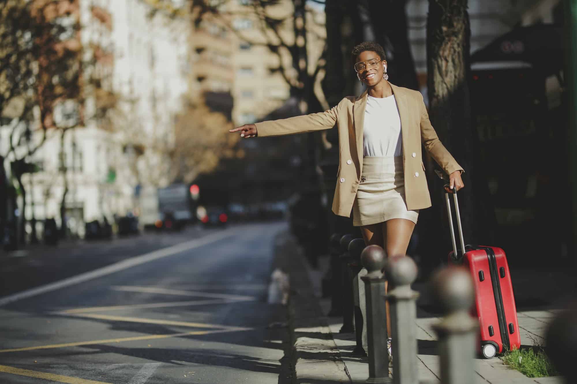 Stylish black woman with luggage hitchhiking on street